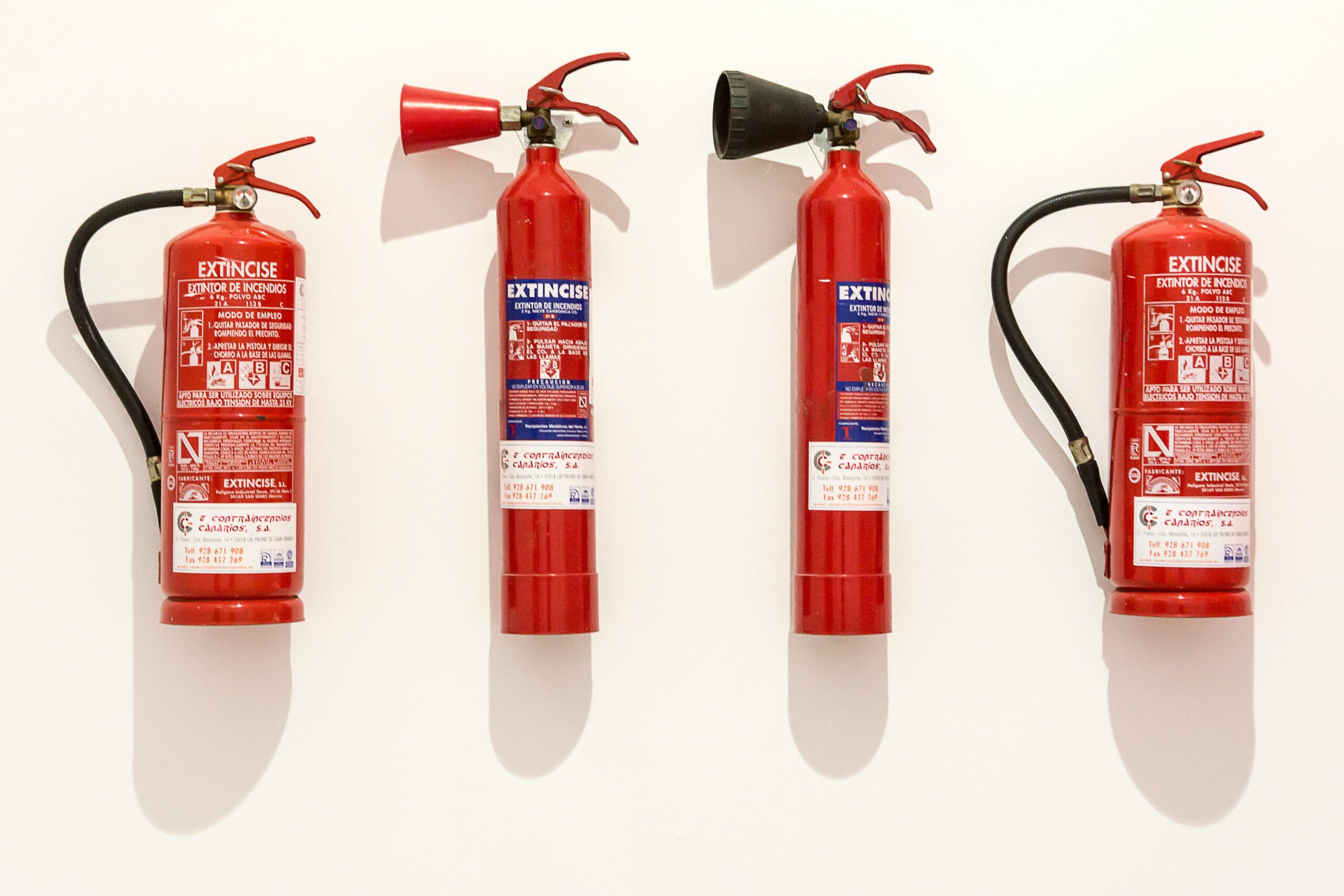 Four red fire extinguishers hanging on a clean white wall in an orderly fashion.